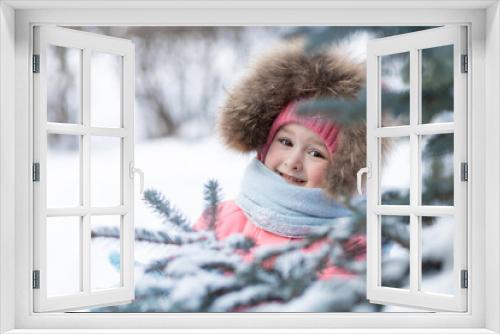 portrait happy little girl in pink jumpsuit playing with snow, snowballs. beautiful child in bright colored clothes in winter near Christmas trees in park, forest. fun winter kids games for children