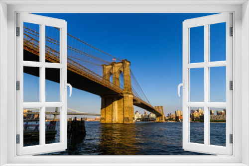Fototapeta Naklejka Na Ścianę Okno 3D - View of the Brooklyn Bridge seen from the East River Greenway in Manhattan with people standing under the bridge on an observation deck 