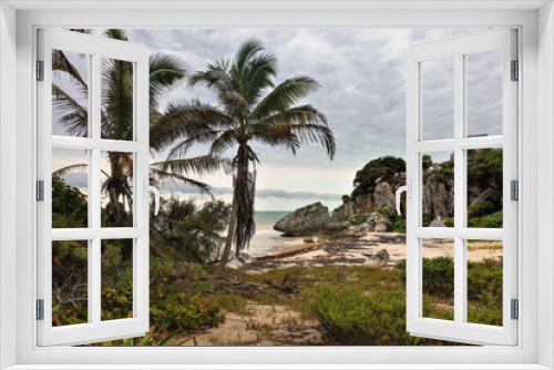 Fototapeta Naklejka Na Ścianę Okno 3D - Beach in the Mayan city of Tulum. On the shore there are tropical vegetation, palms. There are stones and algae on the sand. The ruins of an ancient building are visible on the rocky shore. Mexico