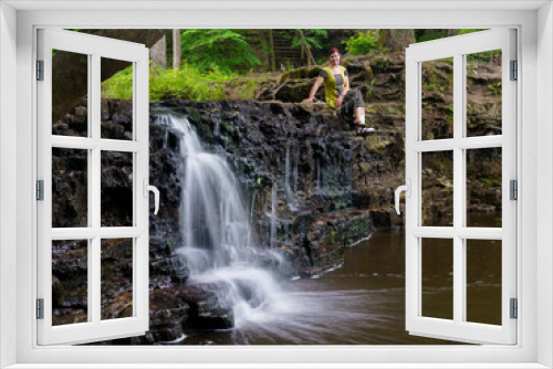 Fototapeta Naklejka Na Ścianę Okno 3D - Waterfall with a small amount of water and a woman sitting on the edge of a half-dried waterfall.

Ivande waterfall with a small stream of water photographed in a long exposure, which allows the water