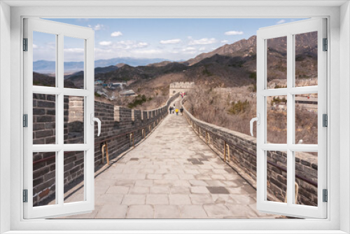 Fototapeta Naklejka Na Ścianę Okno 3D - Beijing, China - April 28, 2010: Great Wall of China. Looking down over landscape on sloped walkway on top of wall which meanders over brown hills under blue cloudscape. Clothing adds bright colors.