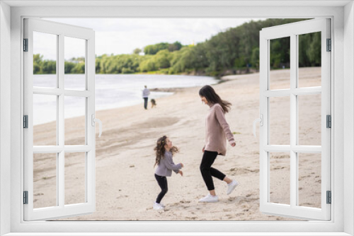 Fototapeta Naklejka Na Ścianę Okno 3D - Cute happy caucasian family of young mother and little daughter jumping and dancing together cheerfully on sandy spring beach outside