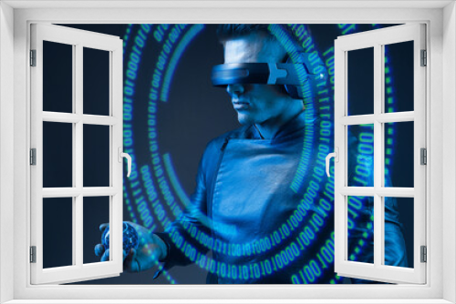 Fototapeta Naklejka Na Ścianę Okno 3D - Man on dark virtual reality background. Guy using VR helmet. Augmented reality, future technology, game concept. Blue neon light. Futuristic holographic interface to display data.