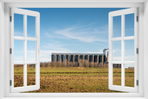 Fototapeta Naklejka Na Ścianę Okno 3D - Large storage silos of an animal feed company on the edge of an agricultural area. The photo was taken on a sunny day in the winter season.