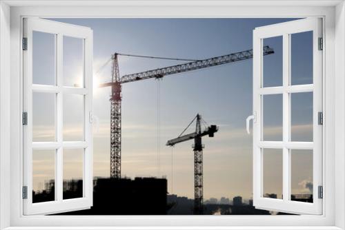 Fototapeta Naklejka Na Ścianę Okno 3D - Silhouettes of construction cranes and unfinished residential building against the sky and shining sun. Housing construction, apartment block in city