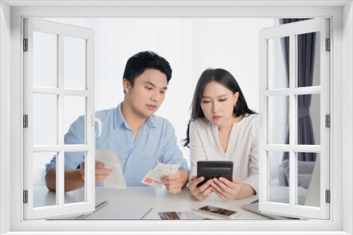 Young Asian couple is calculating their expenses with a home calculator. They feel stressed.