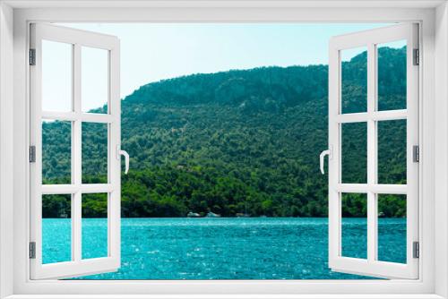 Fototapeta Naklejka Na Ścianę Okno 3D - Summer concept: Many sailing boats and luxury yachts anchored with distance at the Aegean sea. Turquoise sea and green forest background. Natural photo with copy space. No people
