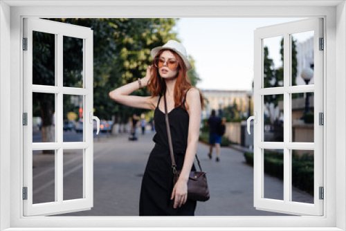 A woman in a black dress and in a white hat with a bag on her shoulder on the street