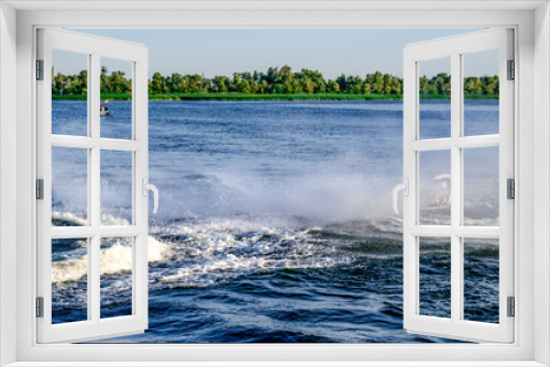 Fototapeta Naklejka Na Ścianę Okno 3D - Splashes and foam on the water of the Dnieper River in Kherson (Ukraine), created by active movements on a jet ski. Beautiful landscape with blue water and green shore on a sunny summer day