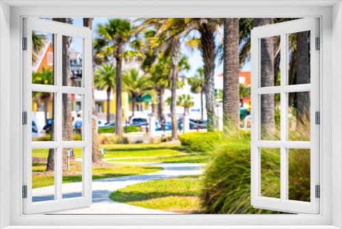 Fototapeta Naklejka Na Ścianę Okno 3D - Green park in St. Augustine, Florida with palm trees and pedestrian paved path with buildings, people in blurry blurred background in sunny summer