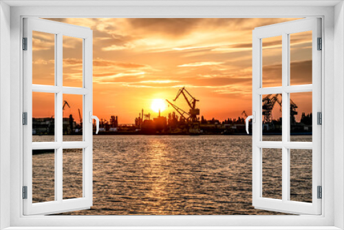Fototapeta Naklejka Na Ścianę Okno 3D - Kherson port at sunset (Ukraine). View from the Dnieper River to the coastline with harbor cranes and commercial ships illuminated by orange sunbeams