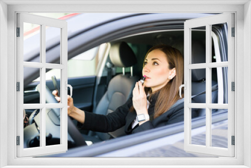 Side view of a beautiful businesswoman putting lipstick in the car