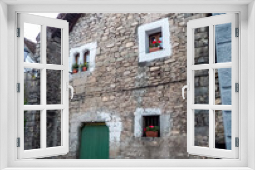 Fototapeta Naklejka Na Ścianę Okno 3D - Fachada de piedra, puerta verde y ventanas con molduras encaladas en la aldea de montaña de Hechó, en los Pirineos españoles