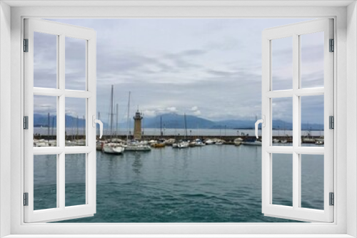 Fototapeta Naklejka Na Ścianę Okno 3D - Cloudy weather on Garda lake, Italy. Picturesque spot in Desenzano del Garda. Yacht, lighthouse, pier, mountains on a background 