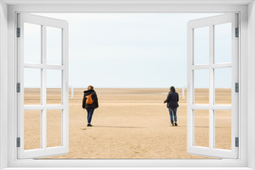 Fototapeta Naklejka Na Ścianę Okno 3D - Two friends meet and go for a walk on the beach at low tide whilst keeping a safe distance apart in accordance with coronavirus restriction rules in England