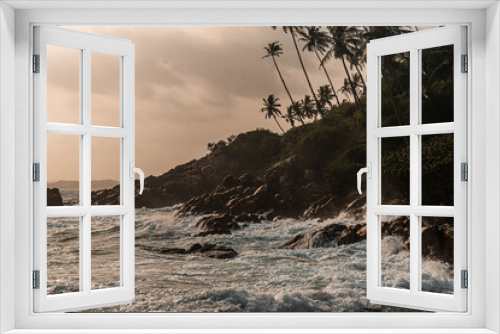 Fototapeta Naklejka Na Ścianę Okno 3D - Skalne wybrzeże na tle oceanu, fal i palm o zachodzie słońca.