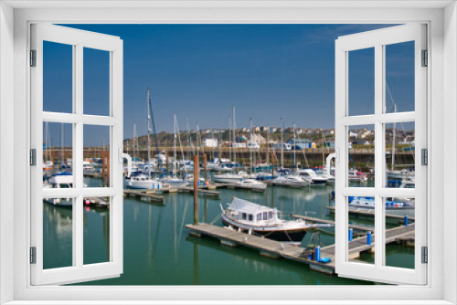 Fototapeta Naklejka Na Ścianę Okno 3D - In sunshine on a calm sunny day, leisure boats moored on piers at Maryport Marina in north west Cumbria, England, UK. In the calm water are reflections of the boats and their masts.