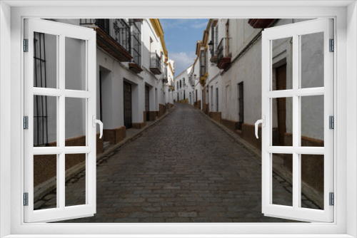 Fototapeta Naklejka Na Ścianę Okno 3D - Alley or narrow street with traditional cobblestone floor and white-walled houses in the famous town of Carmona (Seville, Spain). Empty and quiet street in a town with the typical Andalusian houses.