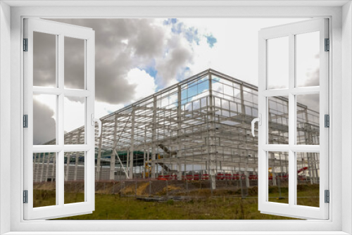 Fototapeta Naklejka Na Ścianę Okno 3D - Metal framework of a partially fabricated large warehouse under construction. Landscape image with space for text. Overcast, clouded skyline. Oxfordshire, England.