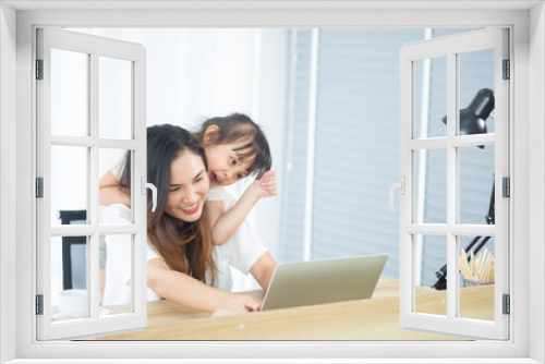 A Happy little Asian daughter and mother look at computer laptop together, have a cheerful expression in house on holiday