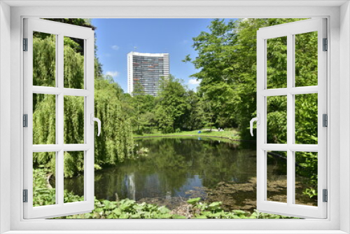 Fototapeta Naklejka Na Ścianę Okno 3D - L'un des étangs entouré de végétation luxuriante et la tour d'habitation Brusillia se reflétant dans l'eau au parc Josaphat à Schaerbeek