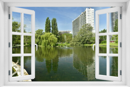Fototapeta Naklejka Na Ścianę Okno 3D - L'étang du parc d'Anderlecht entouré de végétation paysagère luxuriante et l'une des barres principales de l'imposante cité Jules Vives au sud-ouest de la Région de Bruxelles Capitale 