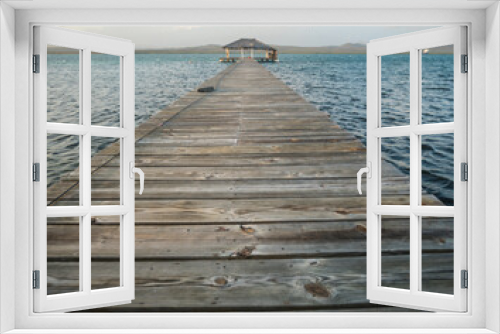 Fototapeta Naklejka Na Ścianę Okno 3D - Dramatic image of old wooden weathered pier leading to the Caribbean bay with a small gazebo and cloudy skies.