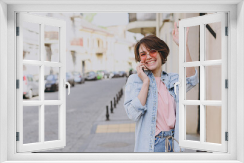 Young smiling caucasian woman 20s in casual jeans clothes eyeglasses talk speby mobile cell phone strolling walk go down city street outdoors, waving hand People youth active urban lifestyle concept