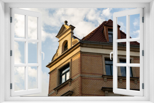 Fototapeta Naklejka Na Ścianę Okno 3D - Facade with yellow clinker bricks in a German city. Sunset sunlight hitting the wall of the building. Old architecture in Germany in front of a blue sky with clouds. European house with red tiles.