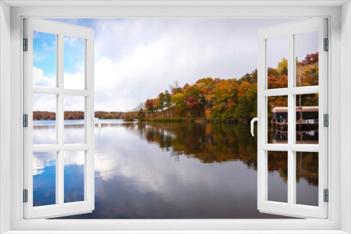 Fototapeta Naklejka Na Ścianę Okno 3D - The wind is calm on a Wisconsin lake in fall.  The colors of the trees and the partly cloudy sky is reflected in the lake's surface.