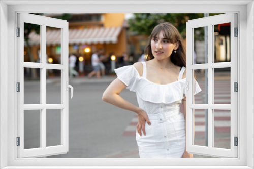 close-up of an attractive brunette woman in a white dress who looks to the side against the backdrop of the street and green trees. the place for your design