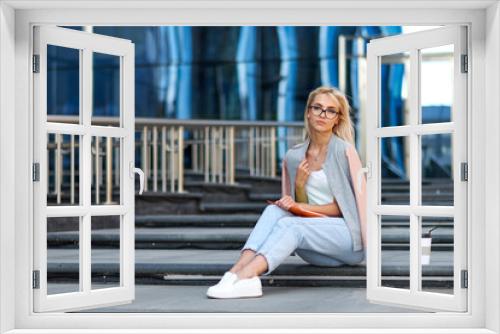 Portrait of an attractive happy woman holding coffee cup while sitting on stairs at the city street