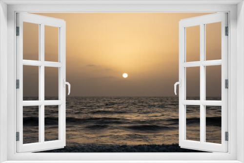 Fototapeta Naklejka Na Ścianę Okno 3D - A view of the orange glow in the sky with sun setting in the horizon and waves in the ocean 