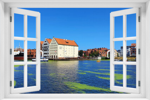 Fototapeta Naklejka Na Ścianę Okno 3D - Gdansk, Poland - July 11, 2021: View of the old city of Gdansk on the Motlawa River. Tourists walk along the waterfront. On Motlawa green patches of duckweed. Middle of the river flows ship.