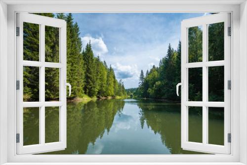 Fototapeta Naklejka Na Ścianę Okno 3D - A river in a spruce forest. a wonderful sunny spring morning. the grassy bank of the river is a white fluffy cloud in the blue sky, a mirror image in the water.