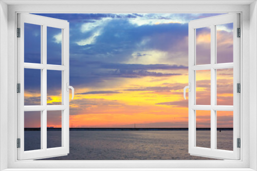 Fototapeta Naklejka Na Ścianę Okno 3D - Beautiful sunset over sea coast. Multicolored blue-violet-orange-yellow sky with curly majestic clouds at sunset. Quiet water. A breakwater on the horizon. Travel vacation holiday relax time concept.