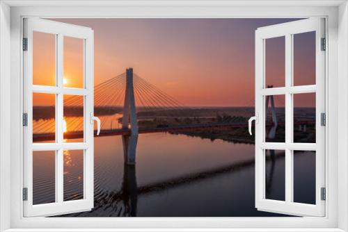 Fototapeta Naklejka Na Ścianę Okno 3D - Aerial view of a white suspension bridge with two huge pillars above a river at sunrise in a rural area
