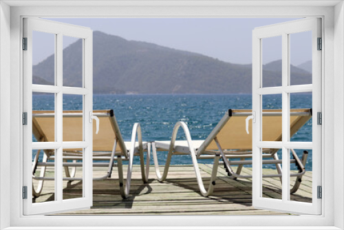 Fototapeta Naklejka Na Ścianę Okno 3D - Sea resort, two empty deck chairs on a wooden pier on green mountains background. Beach vacation on picturesque nature