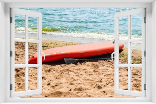 Fototapeta Naklejka Na Ścianę Okno 3D - A red board for sup boarding with a paddle lies on the seashore.