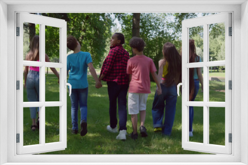 Rear view of diverse teen international friends hold hands walking in park