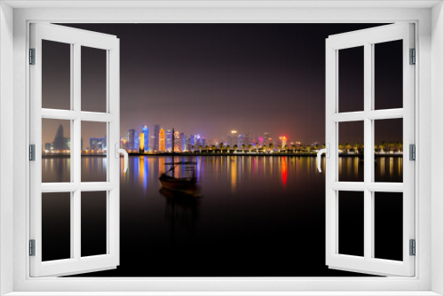 Fototapeta Naklejka Na Ścianę Okno 3D - Illuminated skyline of Doha at night with traditional wooden boat in the foreground, Qatar, Middle East.