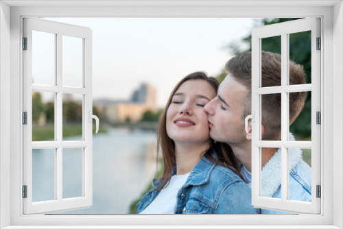 Portrait of young loving couple on river. Guy kisses his beloved on the cheek. Romantic date