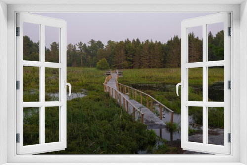 Fototapeta Naklejka Na Ścianę Okno 3D - Wooden boardwalk going through the swamp and marsh leading to the rocky shore and coniferous forest at sunset hour. Grundy Provincial Park Northern Ontario, Canada. Hiking, camping, adventure concept.