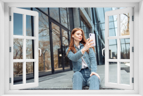 Young pretty woman in headphones and with a smartphone sits on the stairs near the business center