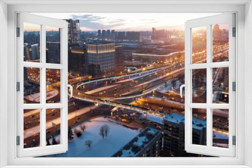 Fototapeta Naklejka Na Ścianę Okno 3D - View from above to Moscow multi-level highway in winter lit by the sunset light. Camera showing panorama of the evining city and then coming closer to the junction with a lot of traffic.