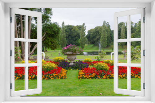 Fototapeta Naklejka Na Ścianę Okno 3D - View through the colourful flower beds down to the lake  with the fountain and woodland background
