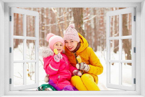 Mom and daughter are walking in the park in winter and eating sausages in dough