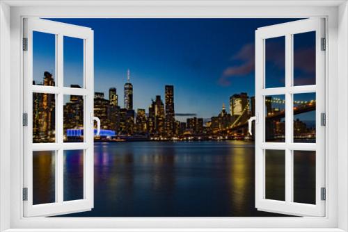 Fototapeta Naklejka Na Ścianę Okno 3D - Stupenda vista notturna dello skyline di New York dal Brooklyn Bridge Park , Manhattan, New York. Fiume con palazzi illuminati come sfondo. Foto Panoramica in lunga esposizione.