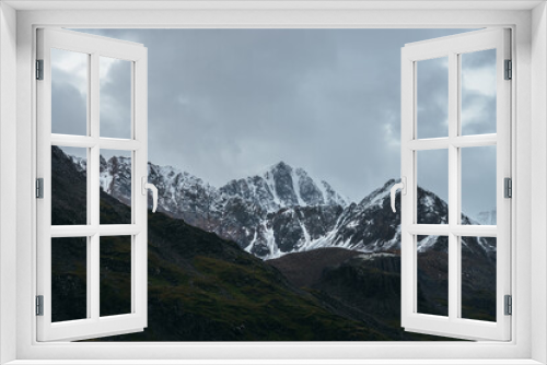 Atmospheric alpine landscape with great mountain peaked top with snow in low clouds. Dramatic mountain scenery with sharp pinnacle in overcast weather. Awesome view to snowy pointy peak in cloudy sky.