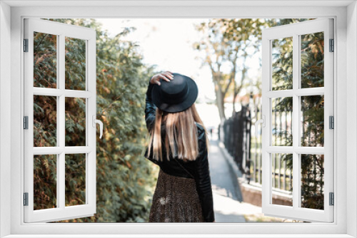 Fototapeta Naklejka Na Ścianę Okno 3D - Beautiful young model girl with long hair in a fashionable leather jacket with a vintage dress and hat travels in the park on a warm autumn day